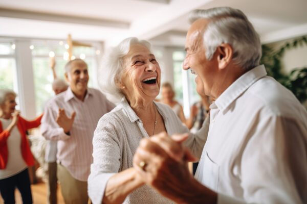 An elderly couple is dancing at a house party in an apartment for elderly friends, smiling and enjoying chatting with friends. Time for the elderly